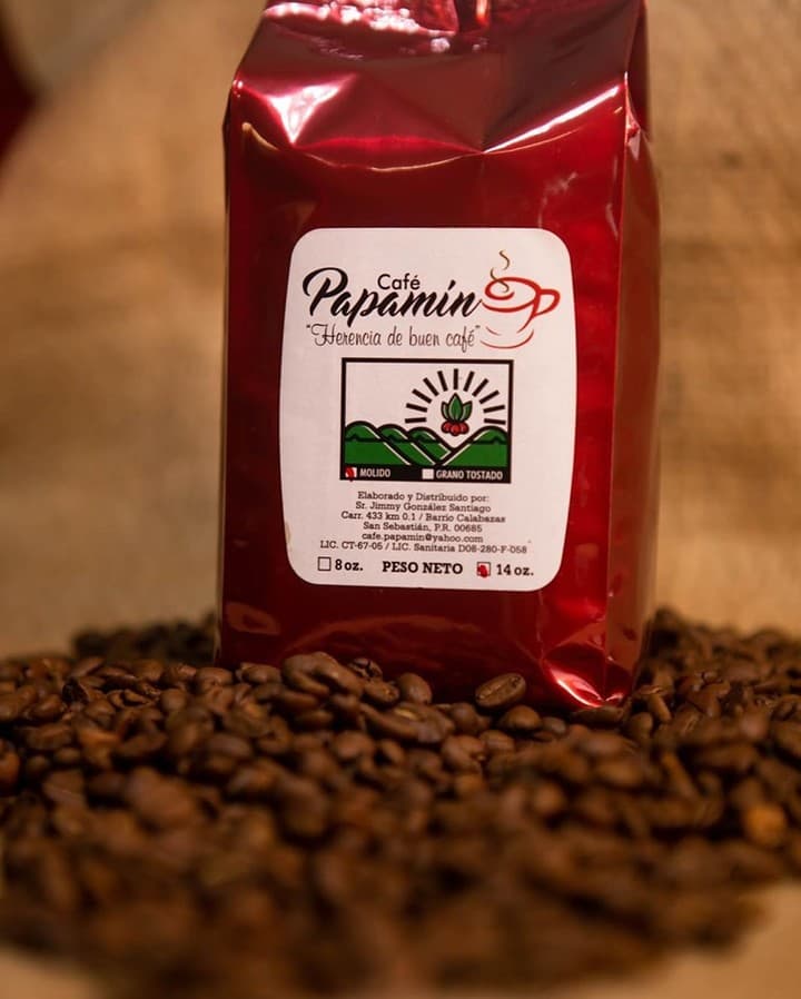 Una bolsa de Café Papamín, con su distintivo empaque rojo y etiqueta 'Herencia de buen café', rodeada de granos de café tostados, lista para ser disfrutada.